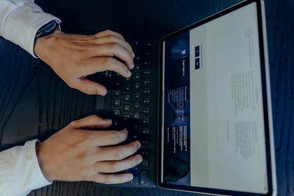 Hender som skriver på et tastatur foran en skjerm som viser tekst.